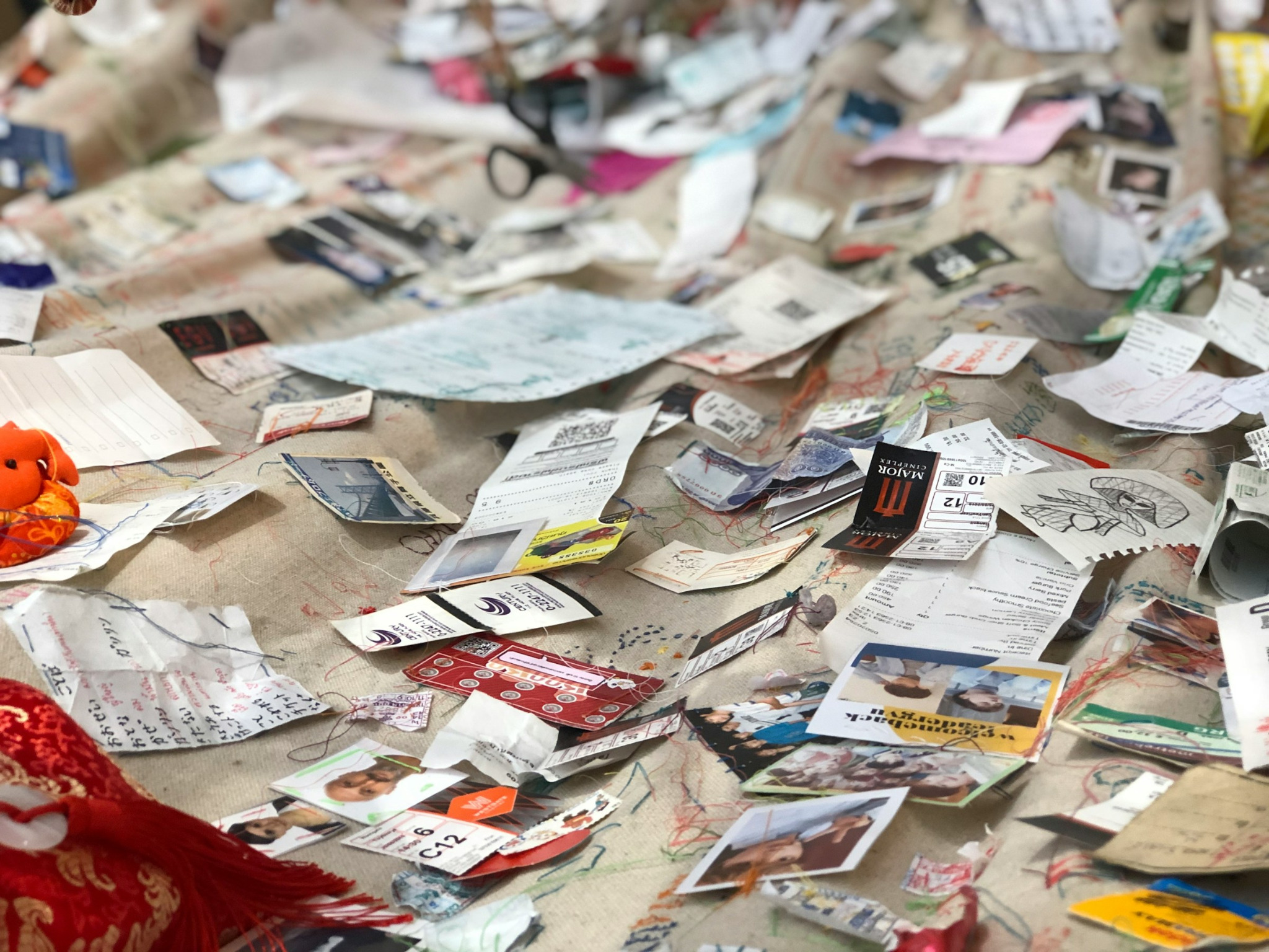 A tabletop scattered with paper fragments, photographs, thread, cloth, notes, and collected creative materials