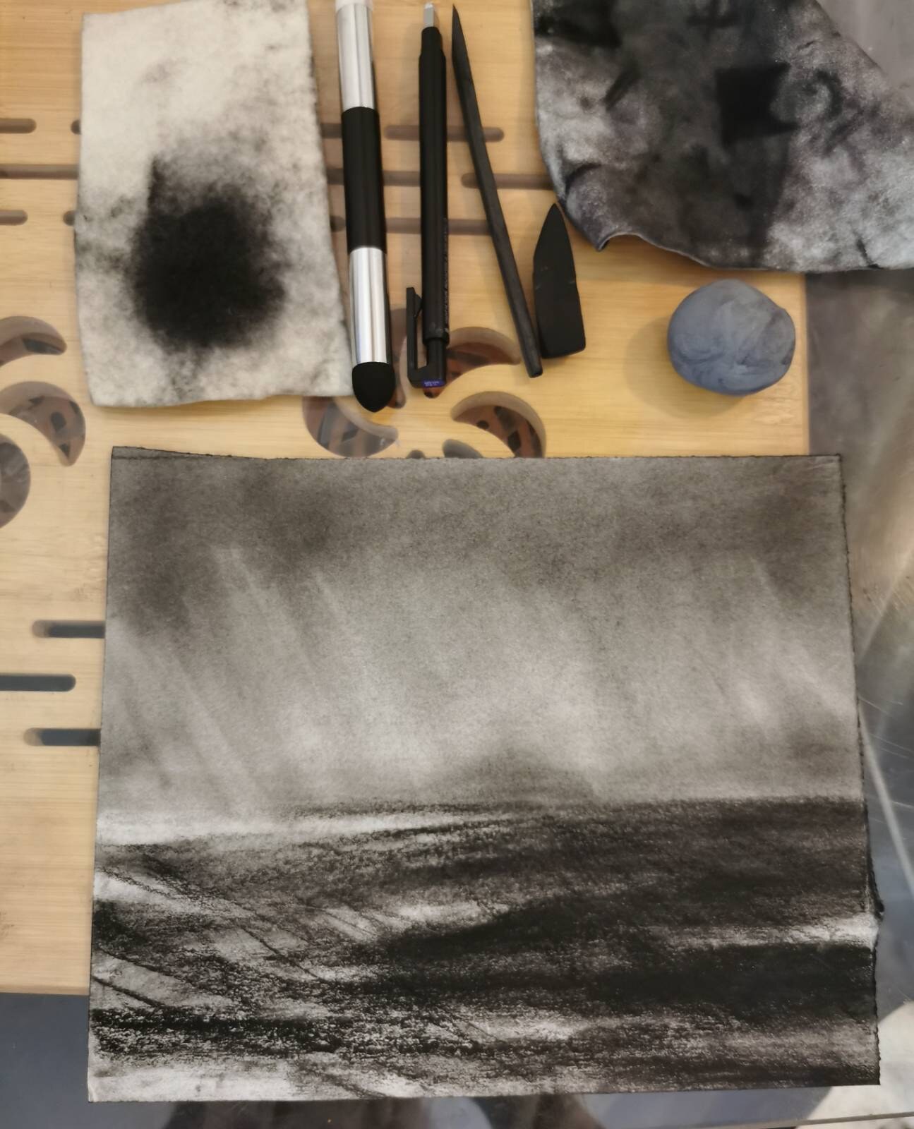 A charcoal seascape study with fog over dark water, surrounded by drawing tools