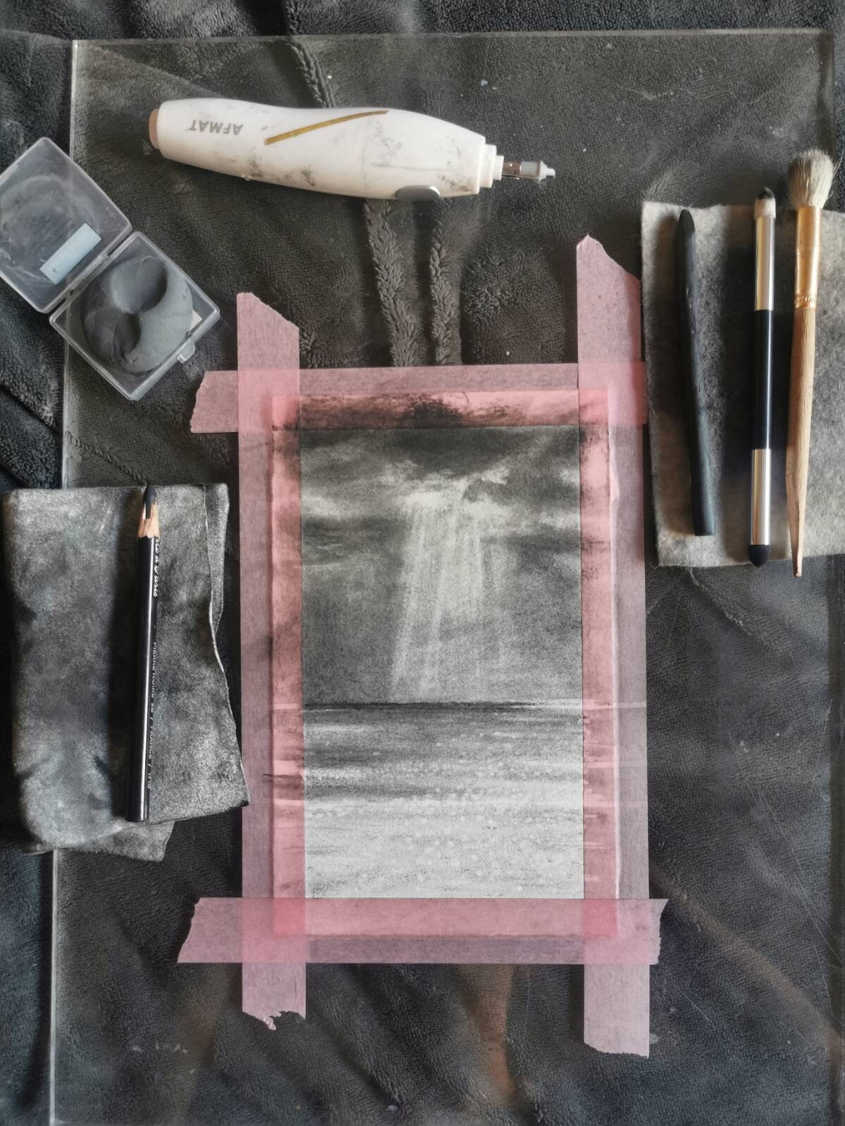A recent charcoal seascape taped down with pink tape and surrounded by charcoal tools