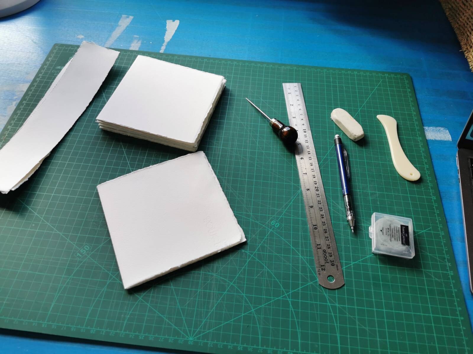 Loose watercolor-paper pages and simple bookbinding tools arranged while making a small sketchbook by hand