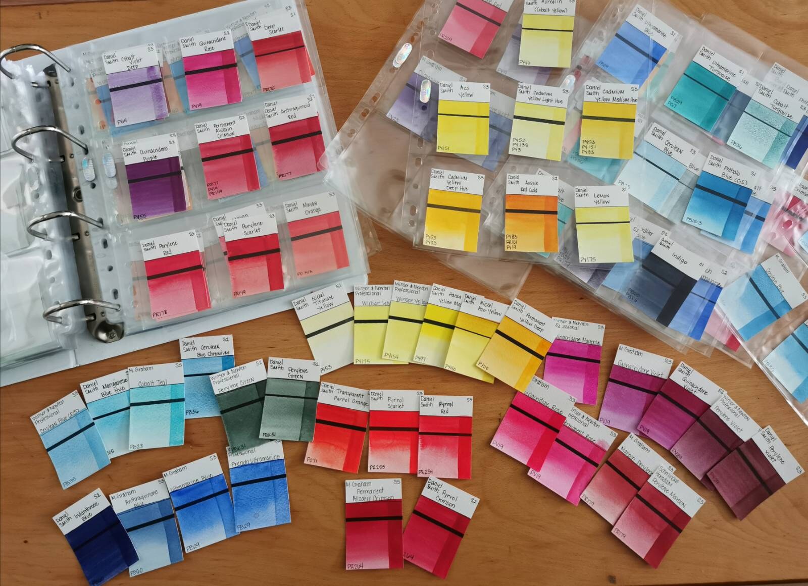 Hundreds of hand-painted watercolor swatch cards sorted into clear binder sleeves and spread across a wooden table