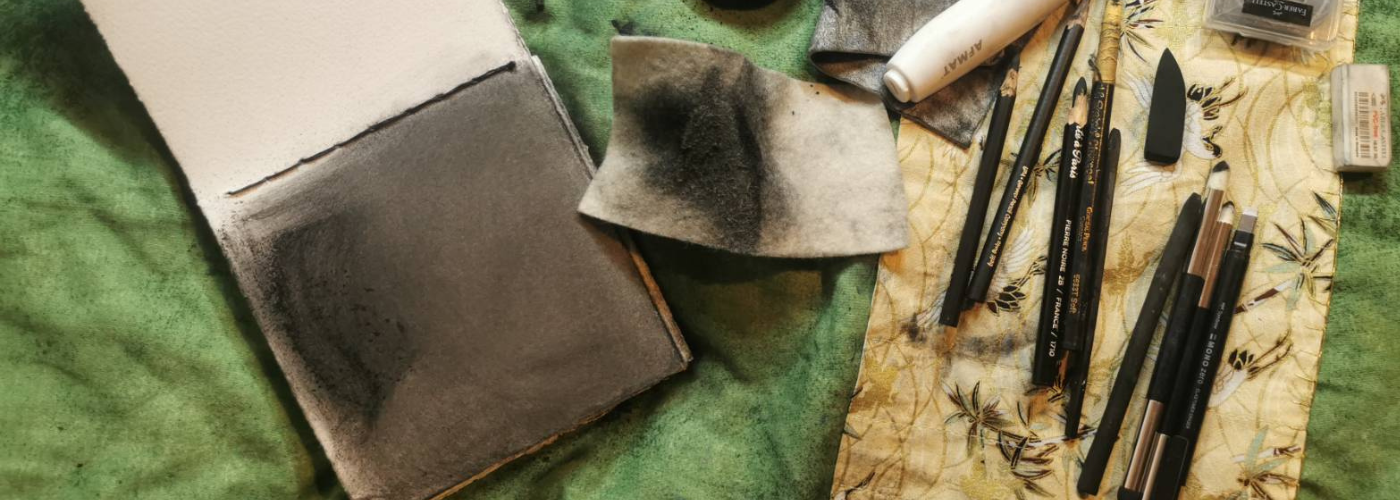 Charcoal drawing, pencils, and brushes arranged on green cloth