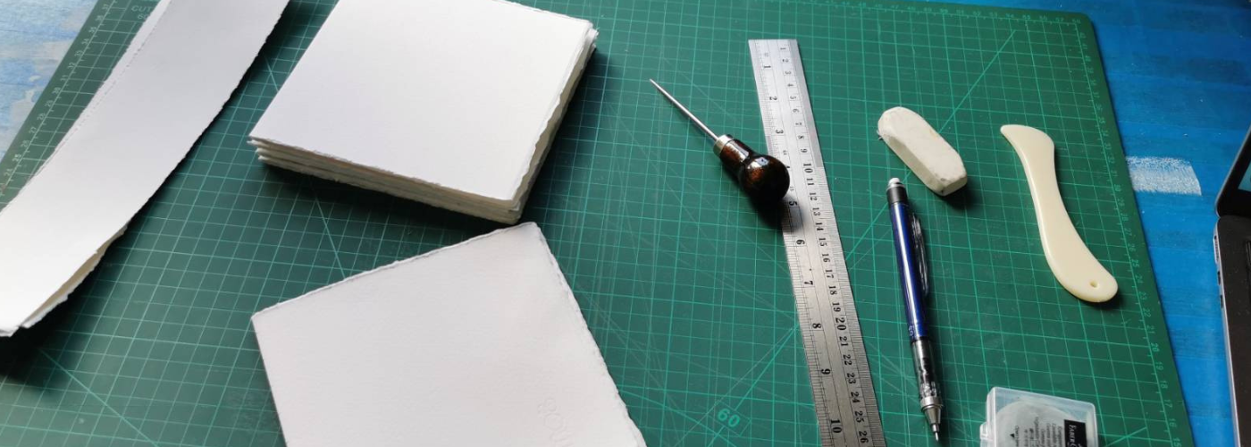 Paper and bookbinding tools arranged on a cutting mat