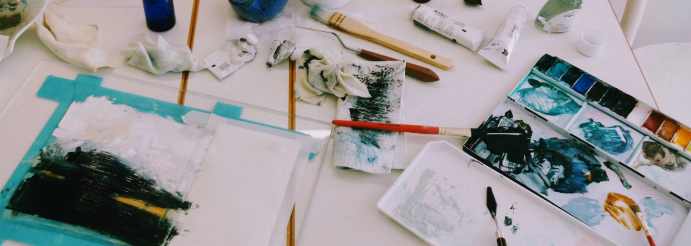 Paints, brushes, and a painting in progress on a studio table